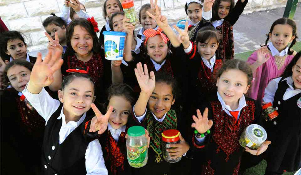 A photograph of a group of Palestinian children in school uniforms smiling for the camera which is above them