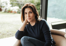 A photograph of Alexandra Lytton Regalado sitting in a chair in front of an open door