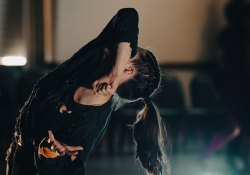 A dancer covers her face with her elbow as she looks up toward the ceiling