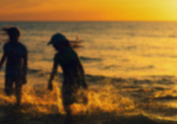 A gauzy photograph of two children playing in the surf. The sun is setting and they are mostly swallowed in shadow