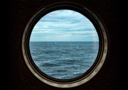 A photograph of a porthole window on a ship, looking out at the ocean