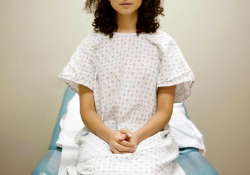A woman in a hospital gown sitting on an examination table with her hands folded in her lap