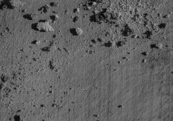 An aerial photo of a gray landscape where rocks cast shadows on the ashen ground below