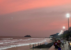 A photograph of a beach at sunset with a lighted highway running past it