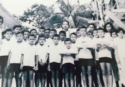 A black and white photograph of a woman standing behind a group of children