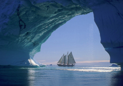 A photograph of a sail boat on the water as seen from inside of an icy cave