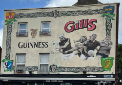 A mural on the side of a building. The mural shows sports figures and the text reads: Guiness. Gills.