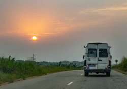 A photograph from behind of a van driving away into the sunset