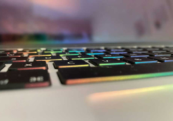 A close-up detail of a computer keyboard that is underlit by rainbow colored LEDs