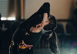 A dancer hides her face behind her elbow as she arcs her back toward the sky