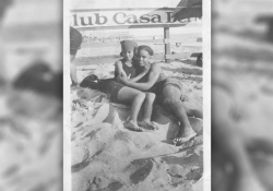 A black and white photo of a man and a woman embracing while they lay in the sand