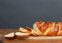 A loaf of baked bread with slices cut off from one end that spill on to the table