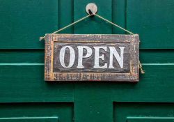 A weather wooden sign that reads, "Open" hanging on a door painted forest green