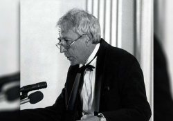 A black and white photograph of Tomas Transtromer talking at a microphone