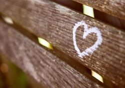 A photograph of a wooden bench with a heart drawn on it in chalk