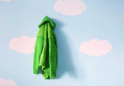 A bright green sweater hanging on a wall painted sky blue with clouds