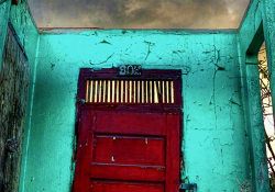 A photograph of a red door inset into a wall that has no roof, with the sky glowering in green-orange above