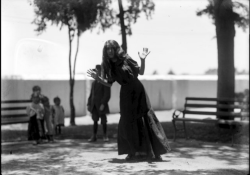 A grainy black and white photo of a woman in a long dress swaying at the waist with her hands up by her face