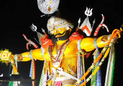 A photo of a Hindu god, wrapped in a turban, strongly lit from below with darkness behind