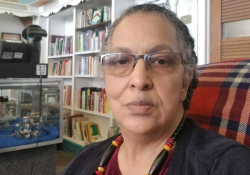 A photograph of a woman sitting in a red plaid chair with a bookstore in the background