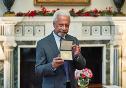 A photograph of Abdulrazak Gurnah holding up his recently awarded medal from the Nobel committee