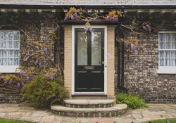 A photograph of a front of a house. The house is built in brick with green plants accenting the stairs leading to the door.