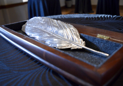 A feather, cast in silver, rests in a velvet lined box