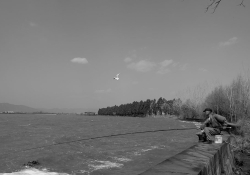 A black and white photo of a man in a business suit perched on the edge of a dam with a fishing pole draped over its edge, the line disappearing into the water below