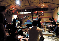 Two men sit with their backs to the camera as a band rehearses