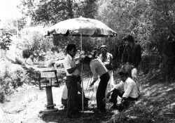 A black and white photograph of men working to secure an umbrella on a film set located in a jungle