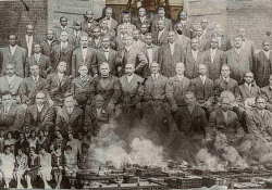 A collage composed of three photos. A black and white photograph of a group of black men dressed in suits. A photo of women similarly posed is overlain in the lower left hand corner and a photo of Tulsa burning overlain in the bottom right hand corner.