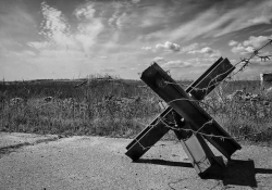 A black and white photo of a cross-shaped road obstacle, wrapped in barbed wire