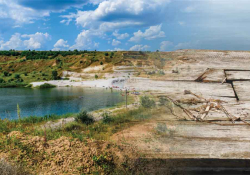 A digital collage. A photograph of a lake bordered by a rocky ridge that blends into a photograph of a worn-wooden raft.