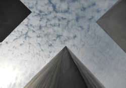 A photograph of a cloud-mottled sky seen from between four looming skyscrapers