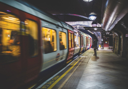 A lone figure stands in the polarized light of the subway at night as a train passes in front of him