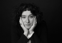 A black and white photograph of a woman, her head resting in her hands, looking soberly at the viewer