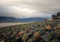 A photo of Svlabard, Noway where a rocky beach in the foregound yields to a bay and foreboding sky in the background