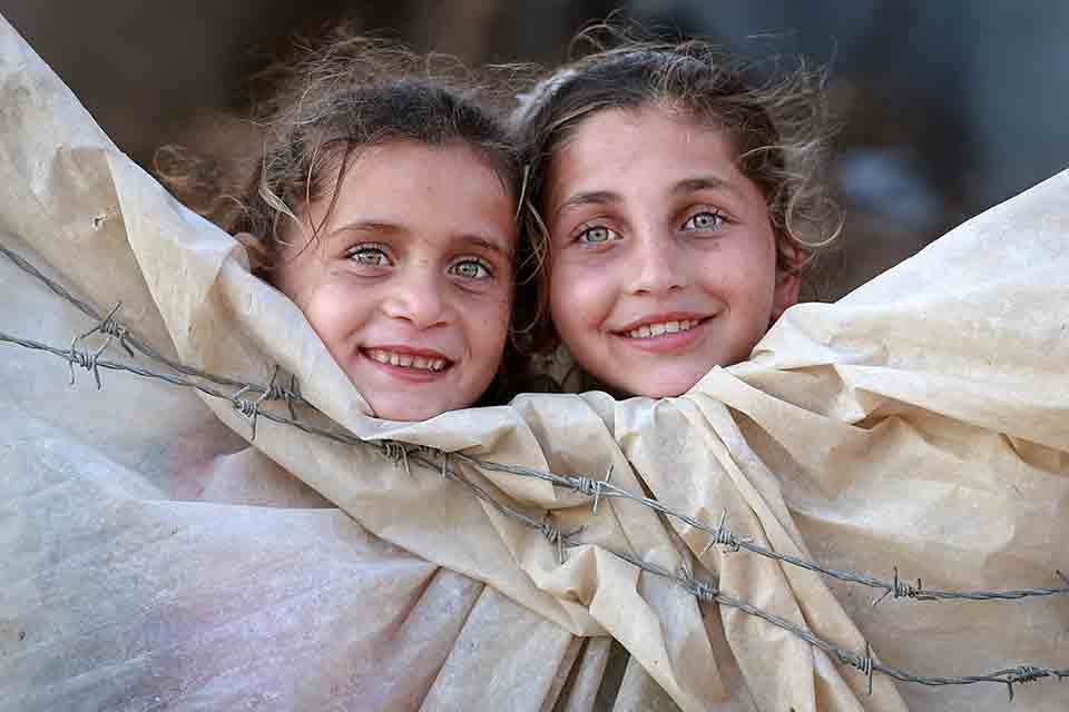 Two children peer out of a canvas tent